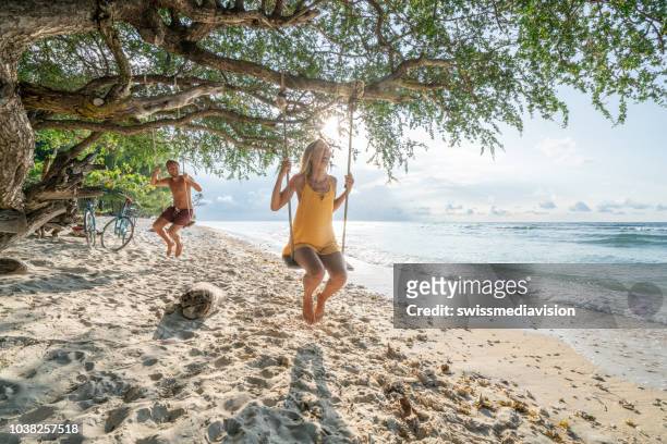 two young adults playing on swing on the beach in tropical paradise, couple having fun happy sharing beautiful moments in perfect vacation time in asia - gili trawangan stock pictures, royalty-free photos & images