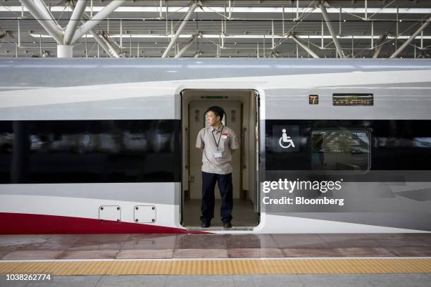 Train attendant stands at a doorway of a Guangzhou-Shenzhen-Hong Kong Express Rail Link Vibrant Express train, operated by MTR Corp., at a platform...