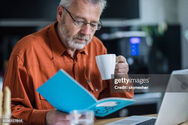 senior man reading while having coffee at home. - engineer reading textbook stock pictures, royalty-free photos & images