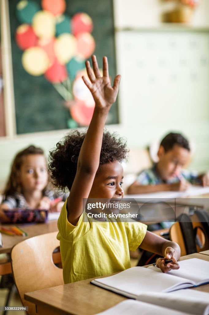 Afro-americano estudante elementar levantando o braço para responder à pergunta em uma classe.