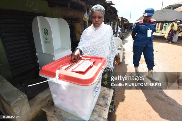 Security officer stands guard near a woman casting her vote outside in the street during the Osun State gubernatorial election in Ede, in the Osun...
