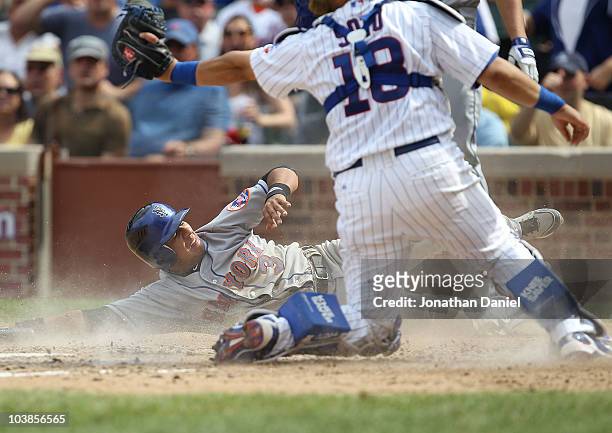 Luis Hernandez of the New York Mets looks up at the umpire after sliding into home past the tag attempt of Geovany Soto of the Chicago Cubs to score...