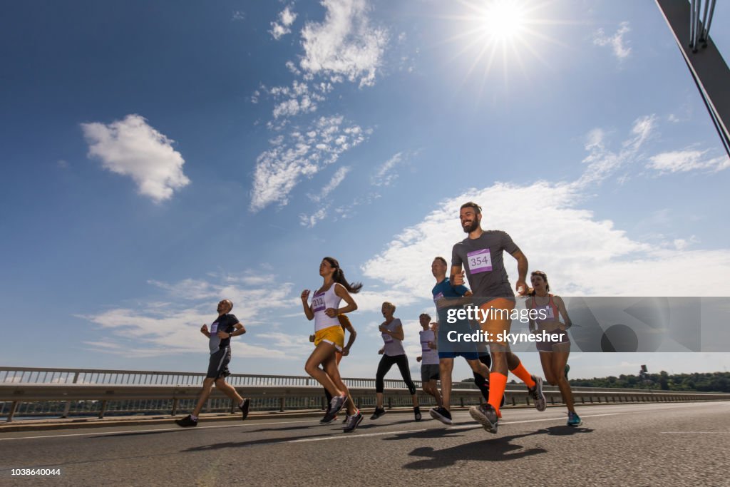 Lage hoek zicht op de grote groep van tevreden atletische mensen lopen van een marathon op de weg.