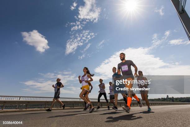 low angle view of large group of happy athletic people running a marathon race on the road. - road running stock pictures, royalty-free photos & images