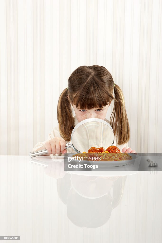 Young girl studying food with magnifying glass