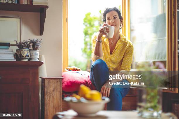 femme d’âge mûr est d’avoir le café du matin à la maison - femme rêveuse photos et images de collection