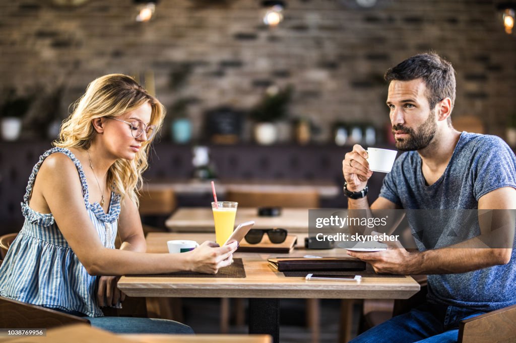 Young couple ignoring each other while sitting in a cafe.