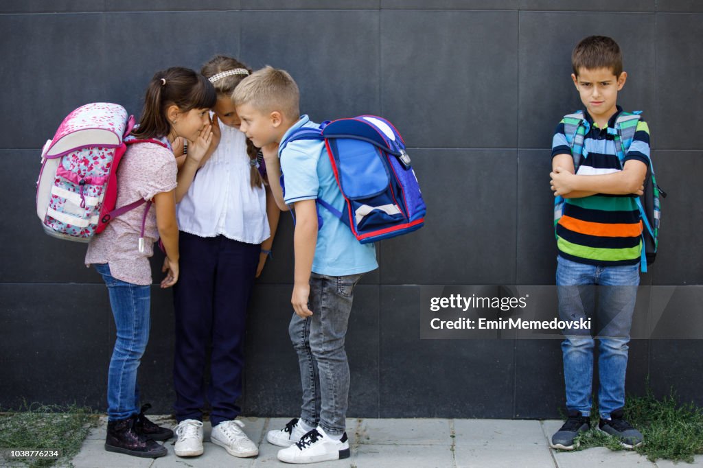 Unhappy boy being gossiped about by school friends