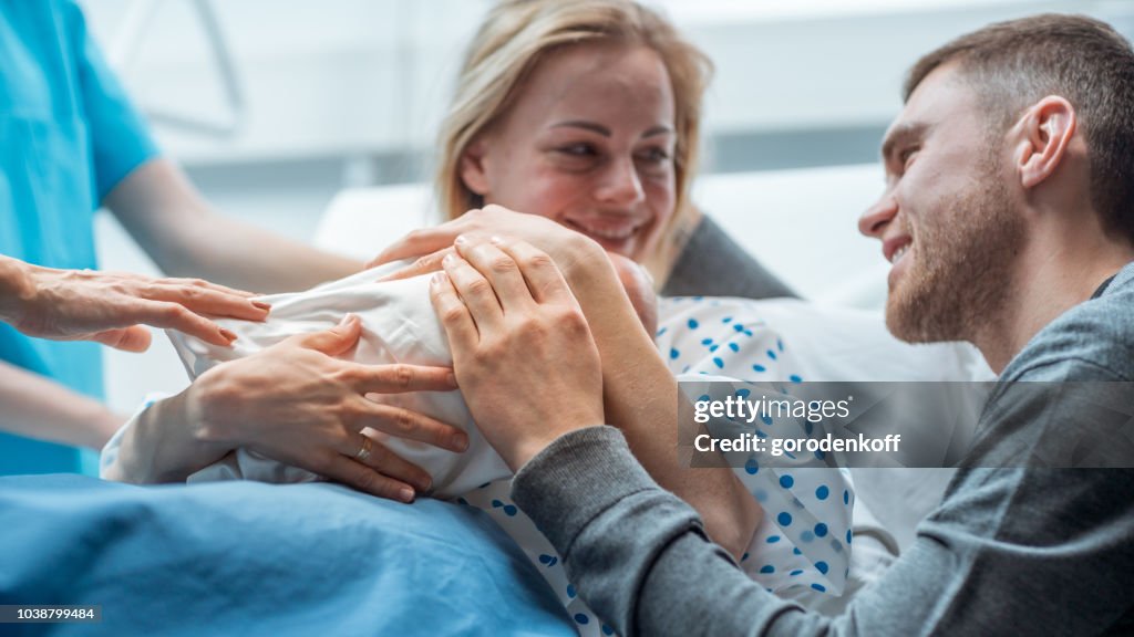 在醫院助產士給了新生兒一個母親舉行, 支援父親親切擁抱嬰兒和妻子。幸福的家庭在現代產房。
