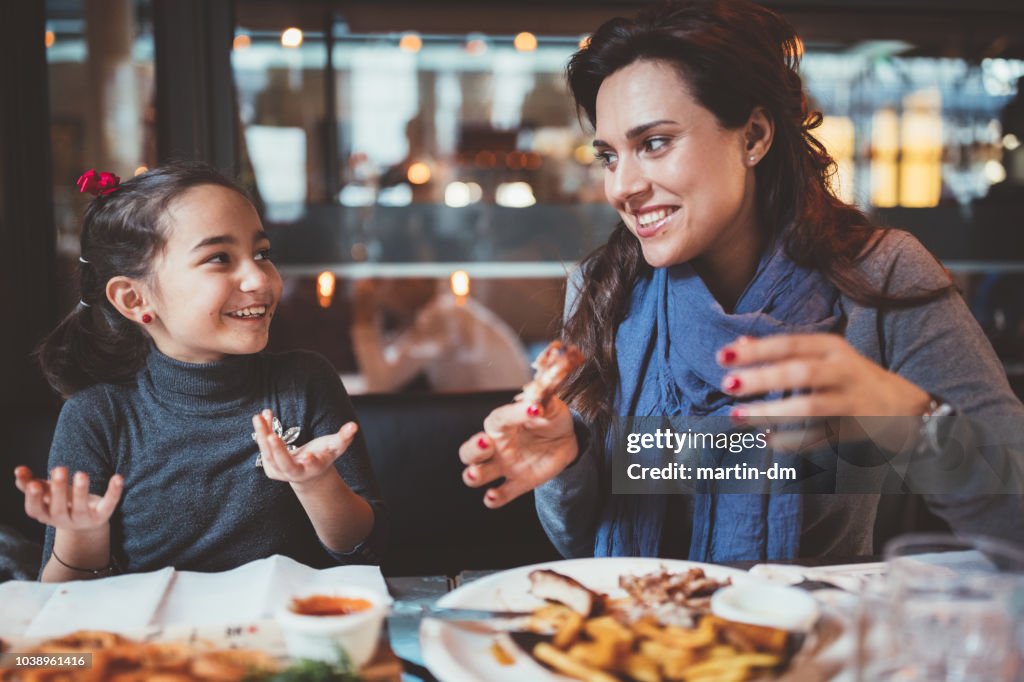 Mother with little daughter eating dinner in restaurant