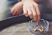 people young man hand putting out a tobacco cigarettes ashtray.,cigarette butt On a wooden bucket.