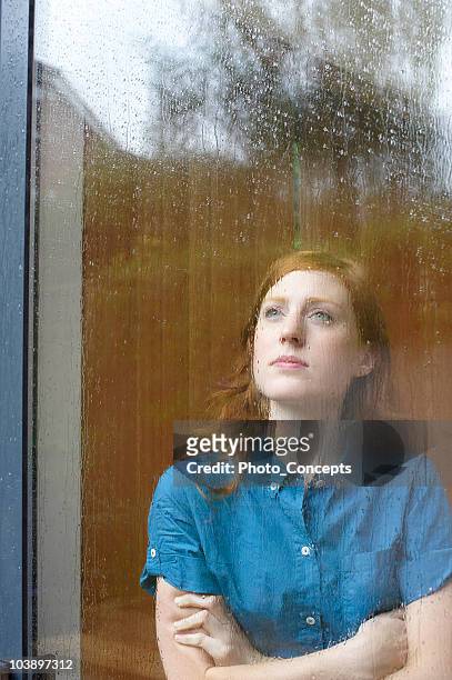 young woman looking out of rainy window - window rain stock pictures, royalty-free photos & images