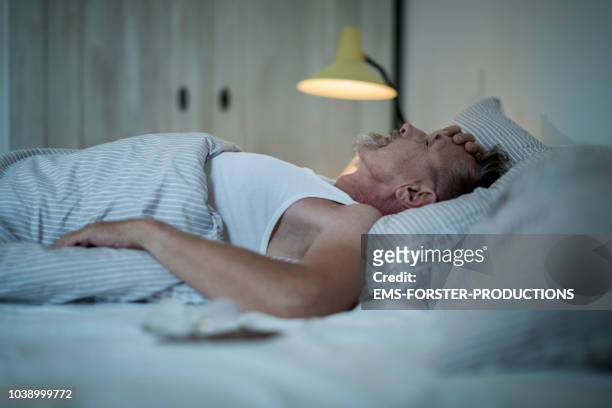 senior man in his early 60s with greying beard is sick and sleepless in bed while night. - white bed stockfoto's en -beelden