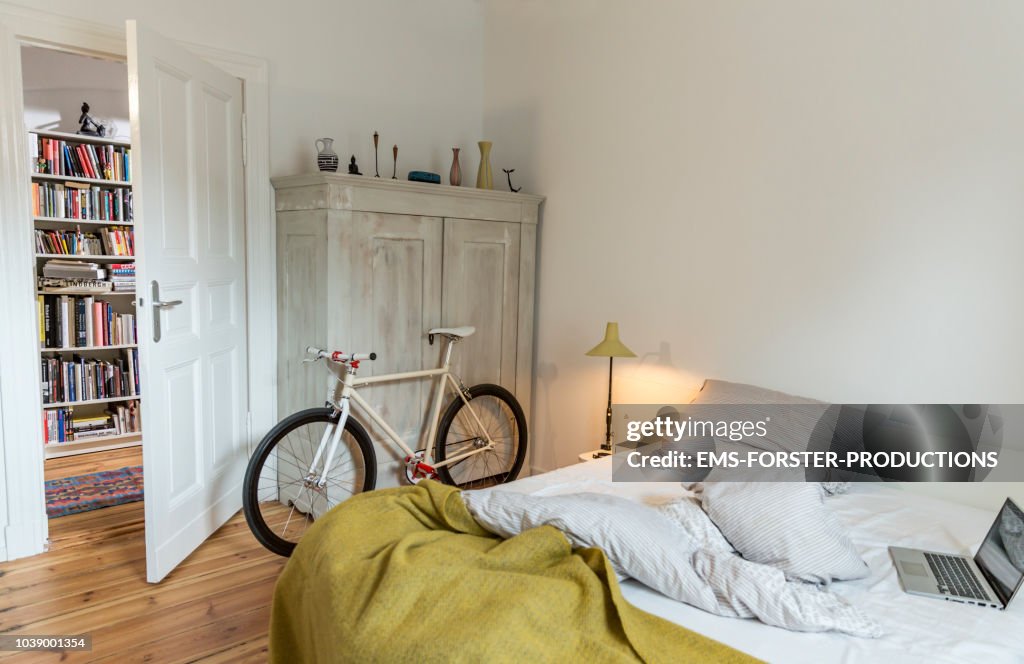 Stylish bedroom witch trendy single speed bike leaning at a cabinet and a laptop on bed.