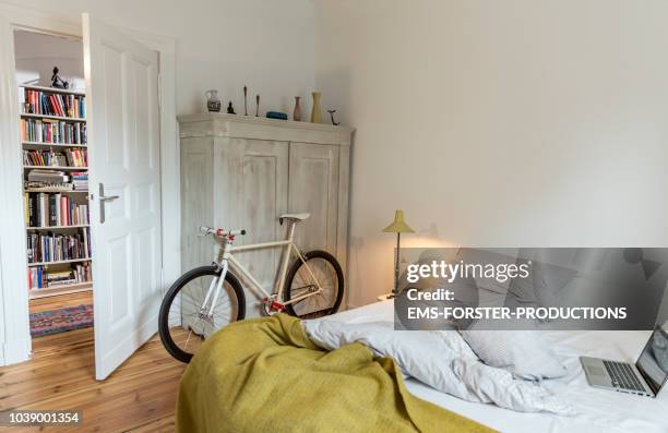 stylish bedroom witch trendy single speed bike leaning at a cabinet and a laptop on bed. - empty bedroom stock pictures, royalty-free photos & images