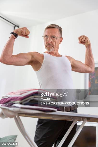 strong semi dressed senior businessman standing behind his ironing board. - vest stock pictures, royalty-free photos & images
