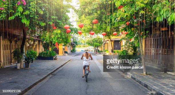 women visiting the old city of hoi an in vietnam by bike during morning - vietnam stockfoto's en -beelden