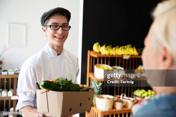young chef with a box full of organic groceries in a local grocery store. - grocer stock pictures, royalty-free photos & images