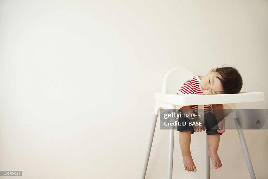 A baby boy sleeping in a high chair 