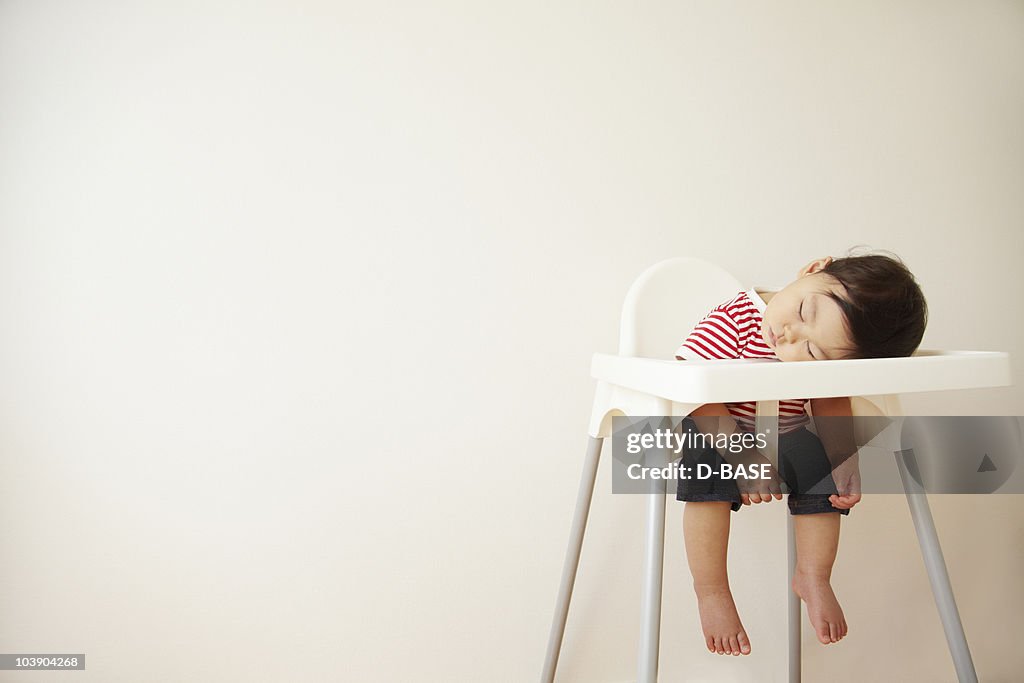 A baby boy sleeping in a high chair