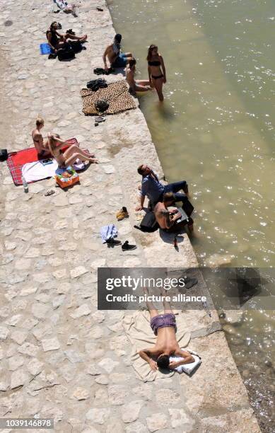 Menschen halten sich am in München in der Nähe der Reichenbachbrücke, am befestigten Ufer der Isar auf und stehen im Wasser, liegen in der Sonne oder...