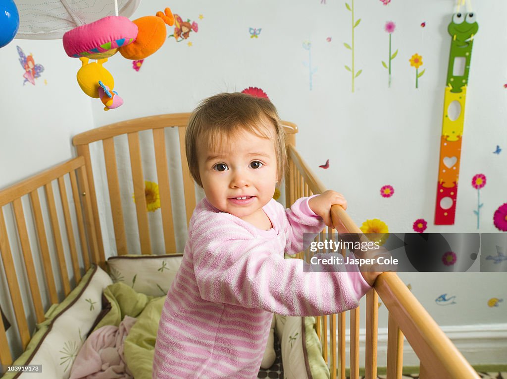 Mixed race baby girl standing in crib