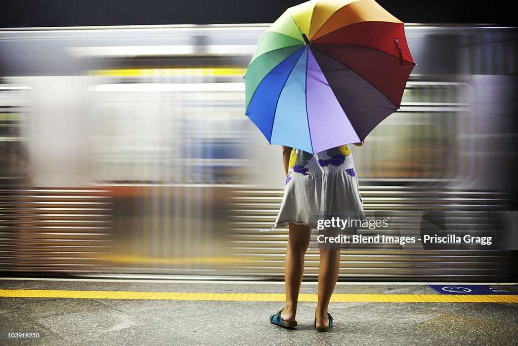 Mixed race woman with umbrella on train platform