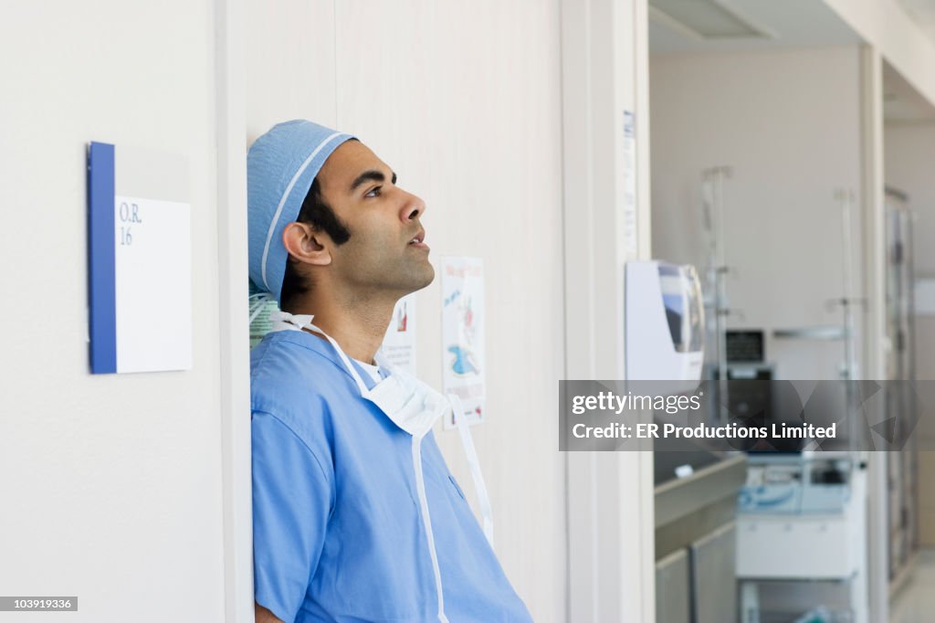 Tired Asian surgeon leaning against wall