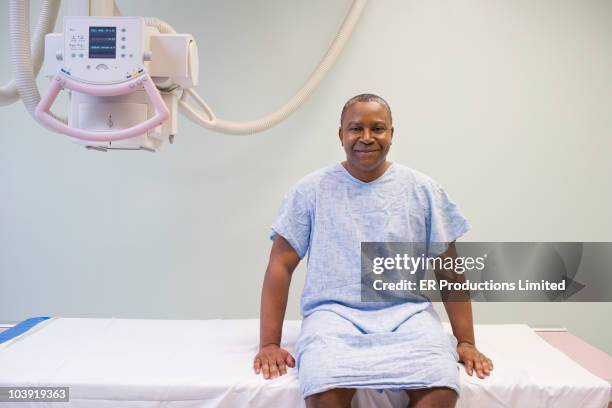 black man in hospital gown sitting on gurney - hospital gown stock-fotos und bilder