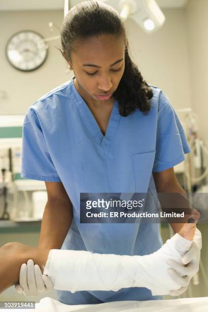 african american doctor treating girl's leg with bandages - african cast broken leg stockfoto's en -beelden