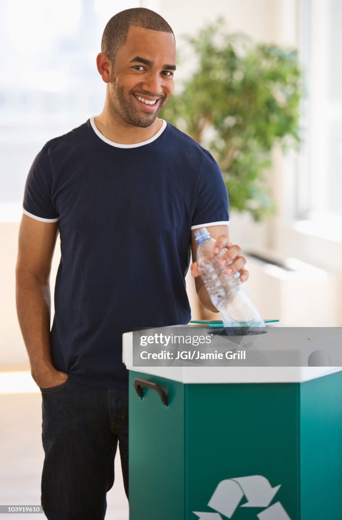 Mixed race man putting plastic bottle in recycling bin