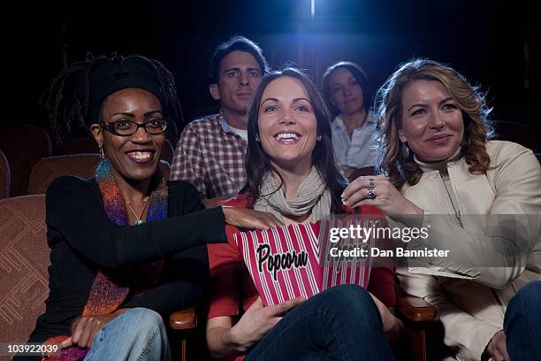 three woman sharing popcorn in movie theatre - five people stock-fotos und bilder