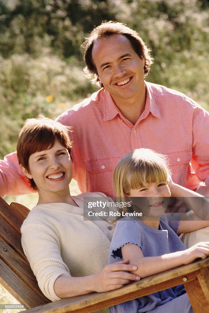 Parents and their young daughter sitting in Adirondack chair