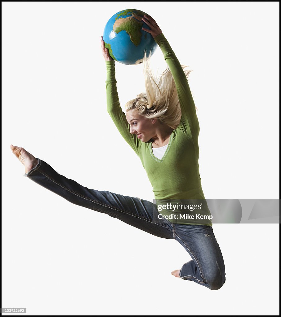Woman jumping in air while holding globe