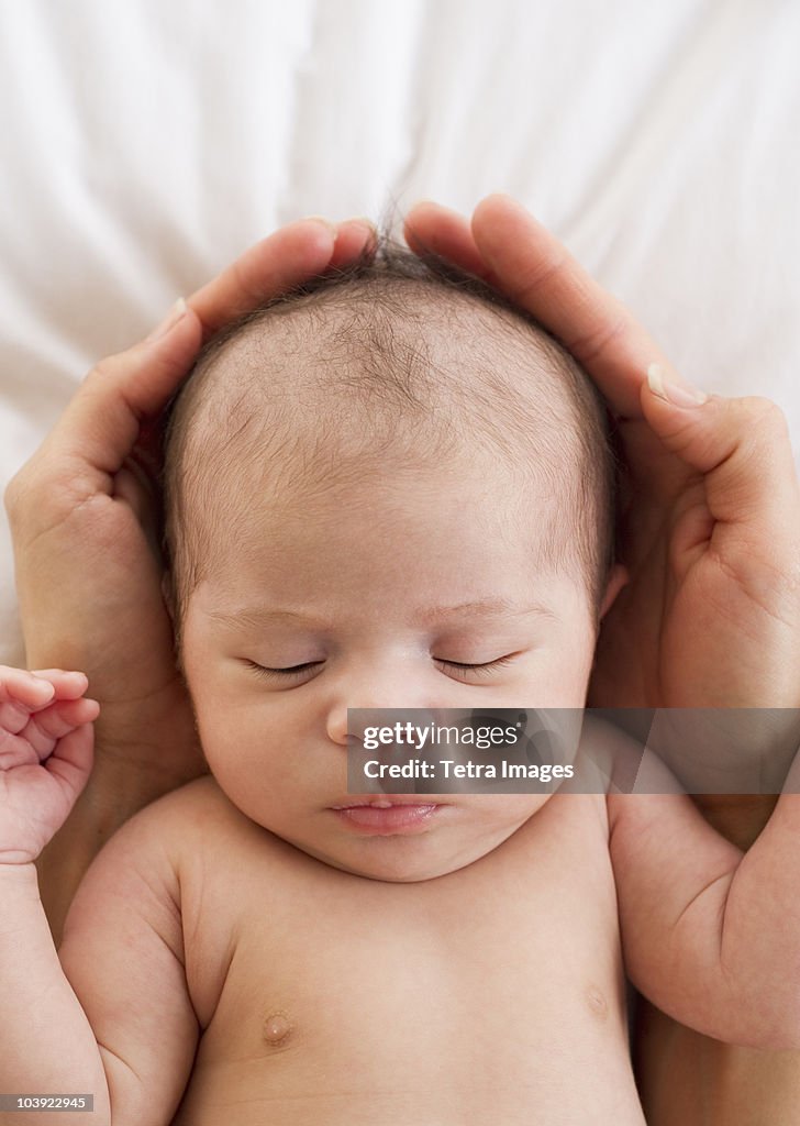 Parent's hands wrapped around sleeping baby's head