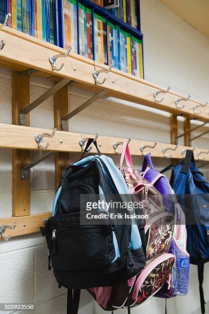 children's backpacks hanging on hooks in classroom - schulrucksack stock-fotos und bilder