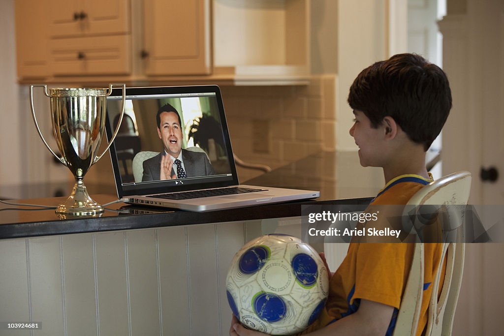 Hispanic boy with soccer ball watching video on laptop
