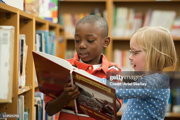 boy and girl classmates sharing book in library - social history fotografías e imágenes de stock