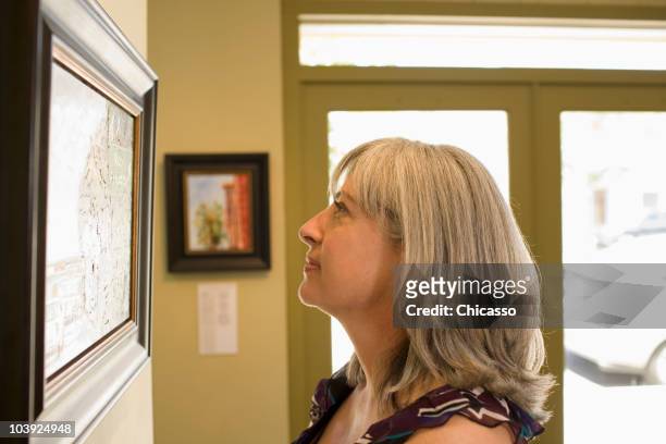 caucasian woman admiring painting in gallery - woman finding grey hair stock pictures, royalty-free photos & images