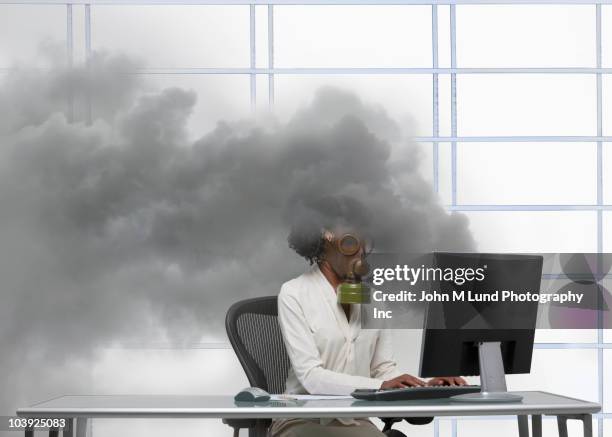 black businesswoman wearing gas mask at smoking computer - hazardous workplace stock-fotos und bilder