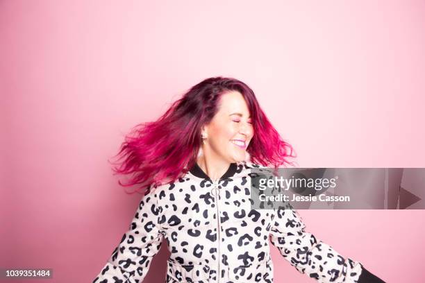 A woman with pink hair dances in front of a pink background