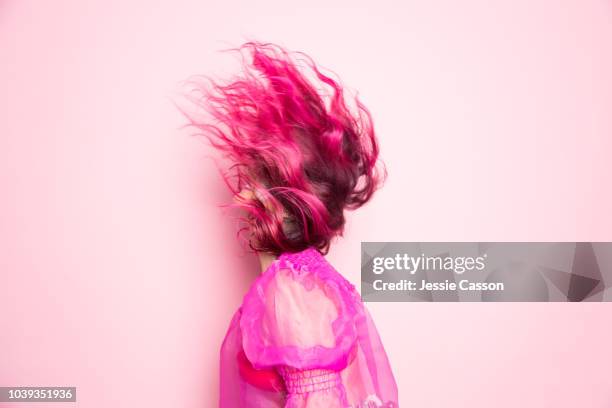 a woman with pink hair throws her head back so that her hair covers her face in front of a pink background - estilista de moda ocupação criativa imagens e fotografias de stock