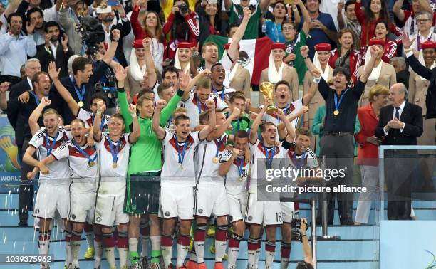 Philipp Lahm of Germany lifts up the World Cup trophy with his teammates Lukas Podolski and Thomas Mueller and head coach Joachim Loew and assistant...