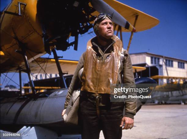 Posed portrait of an unidentified US Navy pilot as he poses in front of an N3N-1 training plane parked on the tarmac at Naval Air Station Pensacola,...