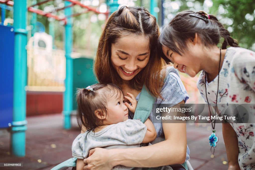Pretty young mom enjoying quality time with her 2 little children in the playground joyfully.
