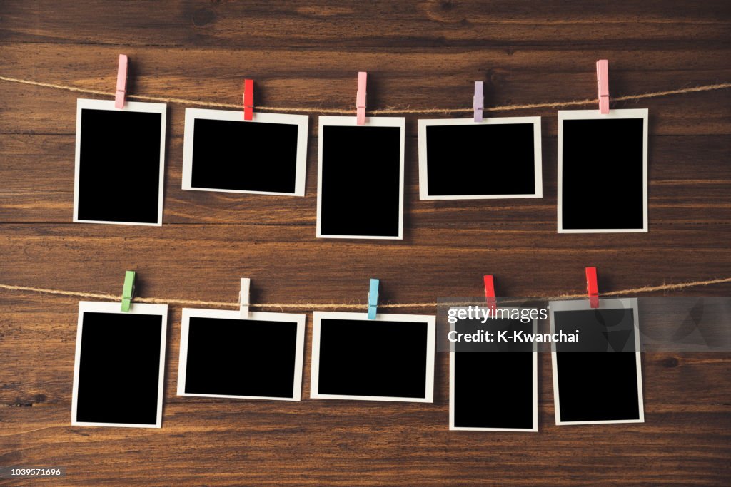 Close-Up Of Blank Instant Print Transfers Hanging With Clothespins On String Against Wooden Wall