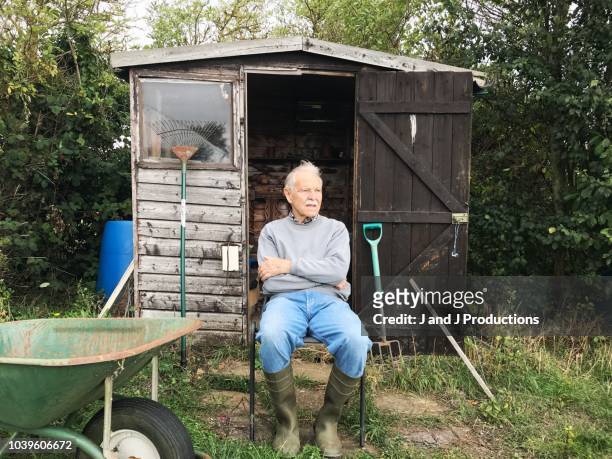 senior man sitting on a chair outside of his garden shed - community garden stock-fotos und bilder