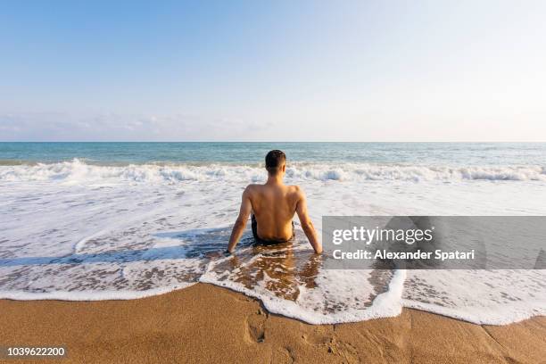 rear view of a young man relaxing at the beach and enjoying waves - barcelona coast stock pictures, royalty-free photos & images