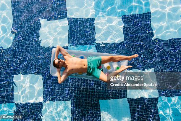 high angle view of a young man in sunglasses sunbathing in swimming pool on inflatable pool raft - 日光浴 ストックフォトと画像