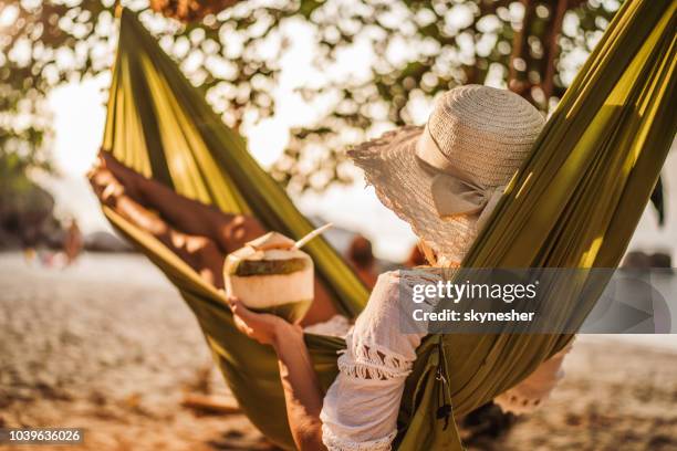 frau mit kokosnuss drink entspannen in der hängematte am strand. - kokosnuss stock-fotos und bilder